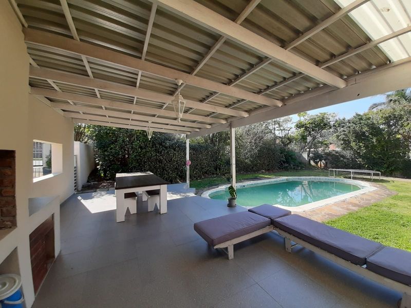 Covered outdoor patio featuring a built-in braai area, overlooking a private swimming pool and garden, ideal for outdoor entertaining.