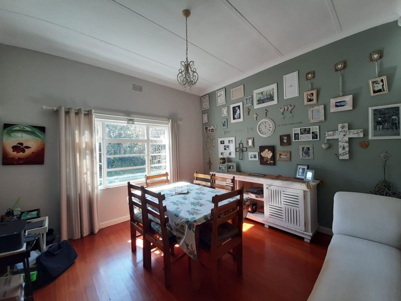 A dining room featuring hardwood flooring, a large window providing natural light, and a decorative ceiling light fixture.