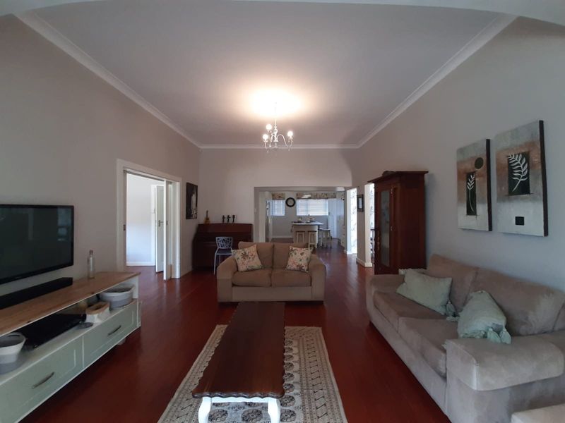 Spacious living room featuring polished hardwood flooring and classic cove cornicing, with an open-plan flow leading towards the kitchen area.