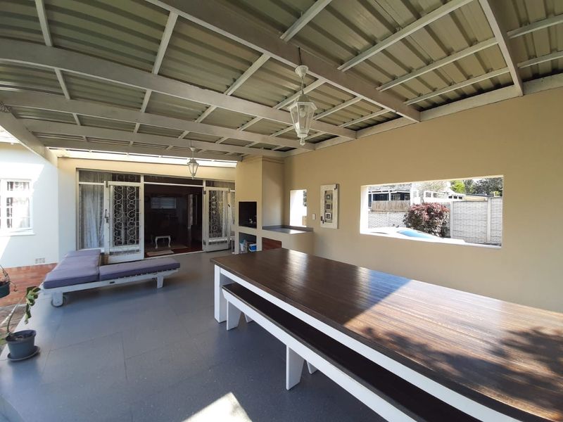 Covered outdoor patio area featuring a built-in braai, metal roof structure, and direct access to the main living space through security gates.