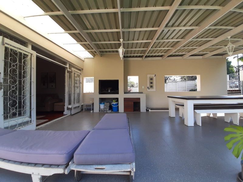 Spacious covered patio featuring a built-in braai, tiled flooring, and translucent roof panels, providing an ideal area for outdoor entertaining.