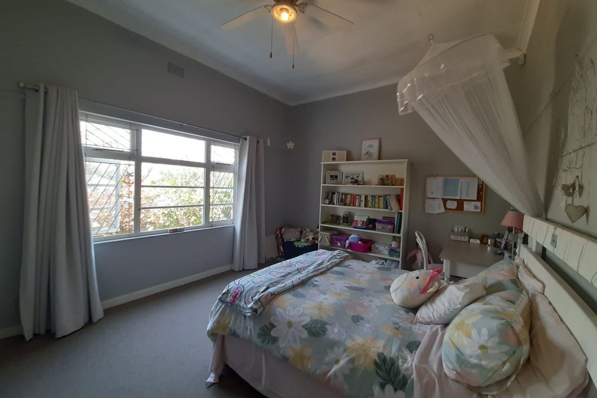 A spacious bedroom featuring a ceiling fan, large window providing natural light, and neutral wall finishes.
