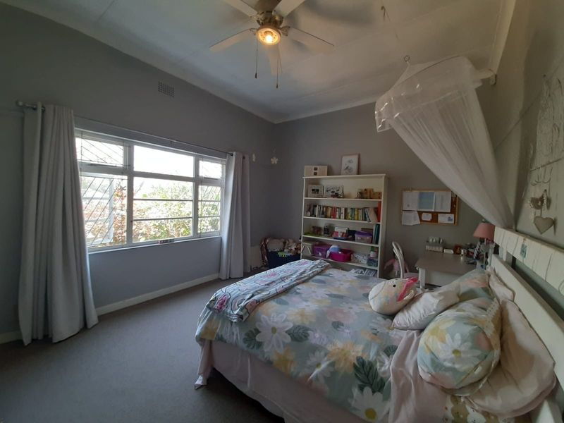 A spacious bedroom featuring a ceiling fan, large window providing natural light, and neutral wall finishes.