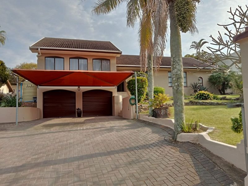 Front elevation of a residential property featuring a double garage with a shade sail, paved driveway, and landscaped garden area.