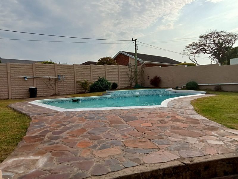 Outdoor pool area featuring a tiled pool surround, water feature, and precast concrete boundary wall.
