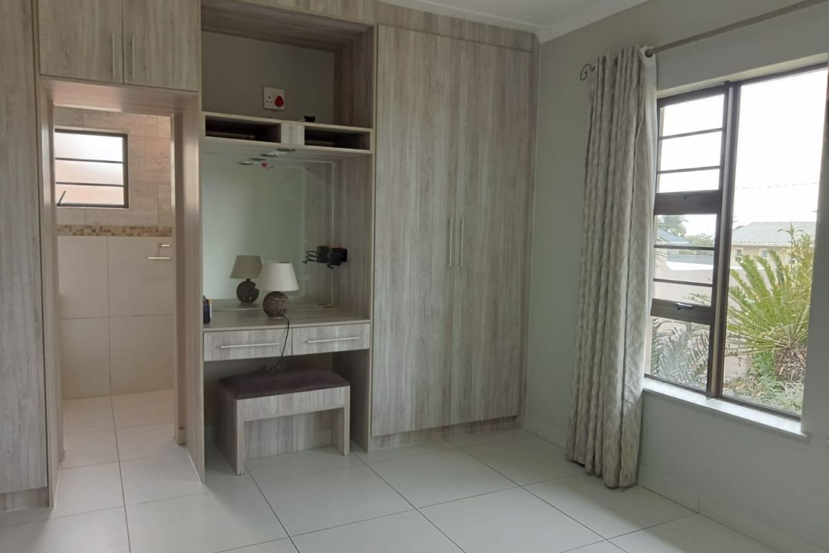 A well-maintained bedroom featuring modern built-in cupboards, a vanity area, tiled flooring, and large windows allowing for natural light.