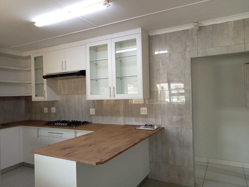 Modern kitchen featuring white cabinetry, wood-look countertops, a gas hob with extractor fan, and neutral tiled backsplash.