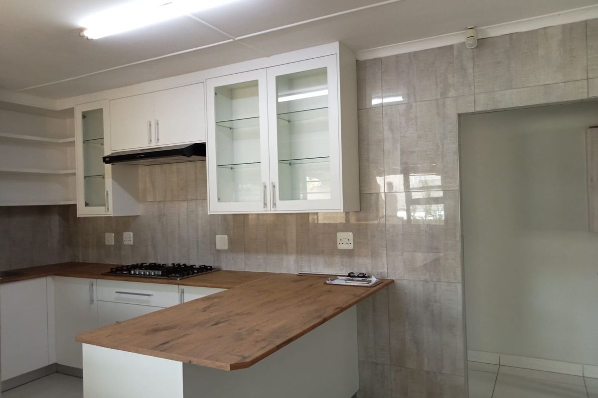 Modern kitchen featuring white cabinetry, wood-look countertops, a gas hob with extractor fan, and neutral tiled backsplash.
