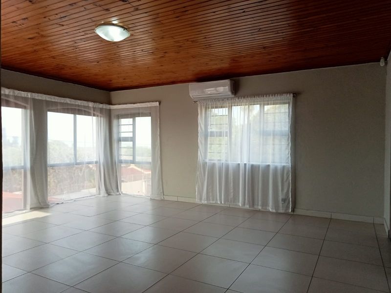 Spacious living area featuring tiled flooring, a timber tongue and groove ceiling, and a wall-mounted air conditioning unit with large windows.