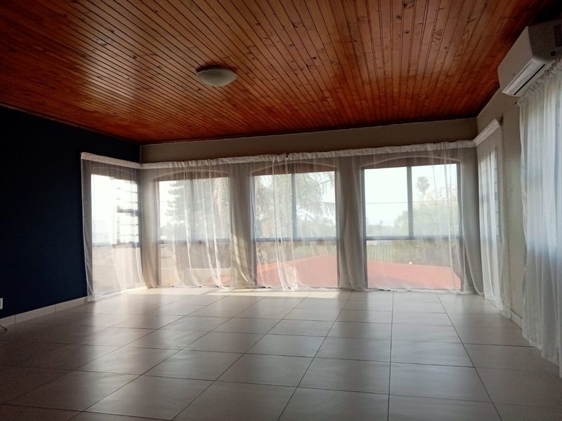 Spacious living area featuring ceramic floor tiles, a warm timber tongue and groove ceiling, and large arched windows providing ample natural light.