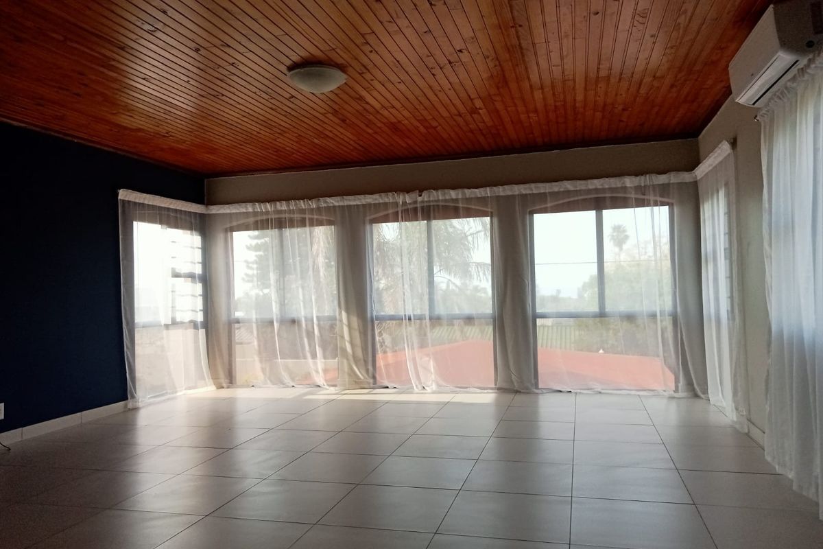 Spacious living area featuring ceramic floor tiles, a warm timber tongue and groove ceiling, and large arched windows providing ample natural light.