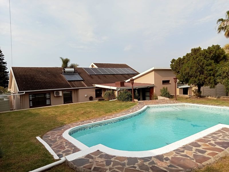 Rear exterior view featuring a swimming pool with stone paving, solar panels, and solar water heating system installed on the tiled roof.