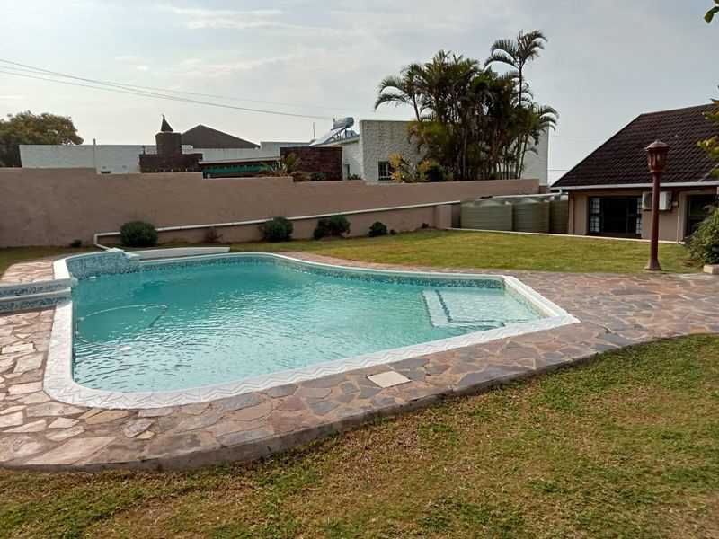 Outdoor pool area featuring a swimming pool with stone paving, surrounding lawn, and boundary wall with water storage tanks.