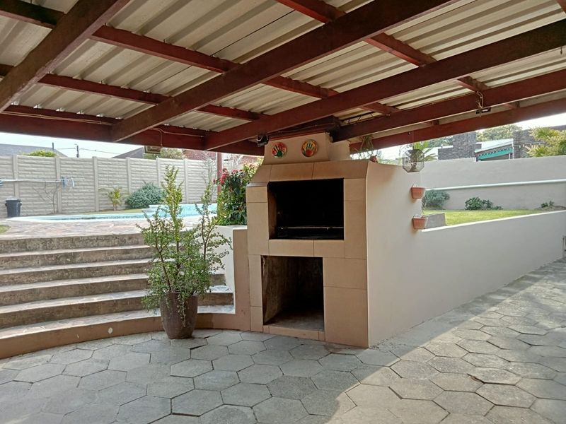 Covered outdoor patio featuring a built-in braai, paved flooring, and direct access to the garden and pool area.