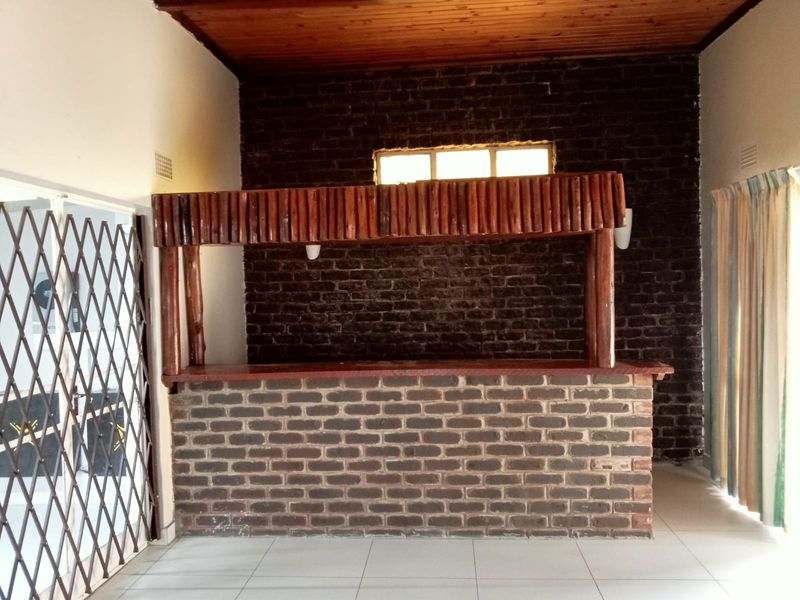A dedicated bar area featuring a built-in brick counter, timber canopy, exposed brick feature wall, and timber ceiling.