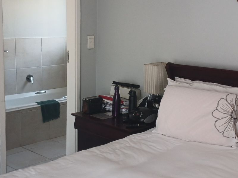 A bedroom view looking into an en-suite bathroom featuring a built-in bathtub and neutral wall tiling.