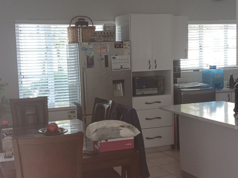 Open plan kitchen and dining area featuring white cabinetry, a central island, and tiled flooring with natural light from venetian blinds.