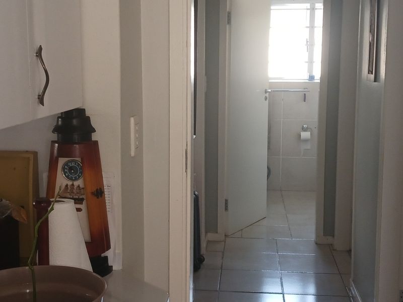 A view through a hallway leading towards a bathroom, featuring tiled flooring and built-in cabinetry.
