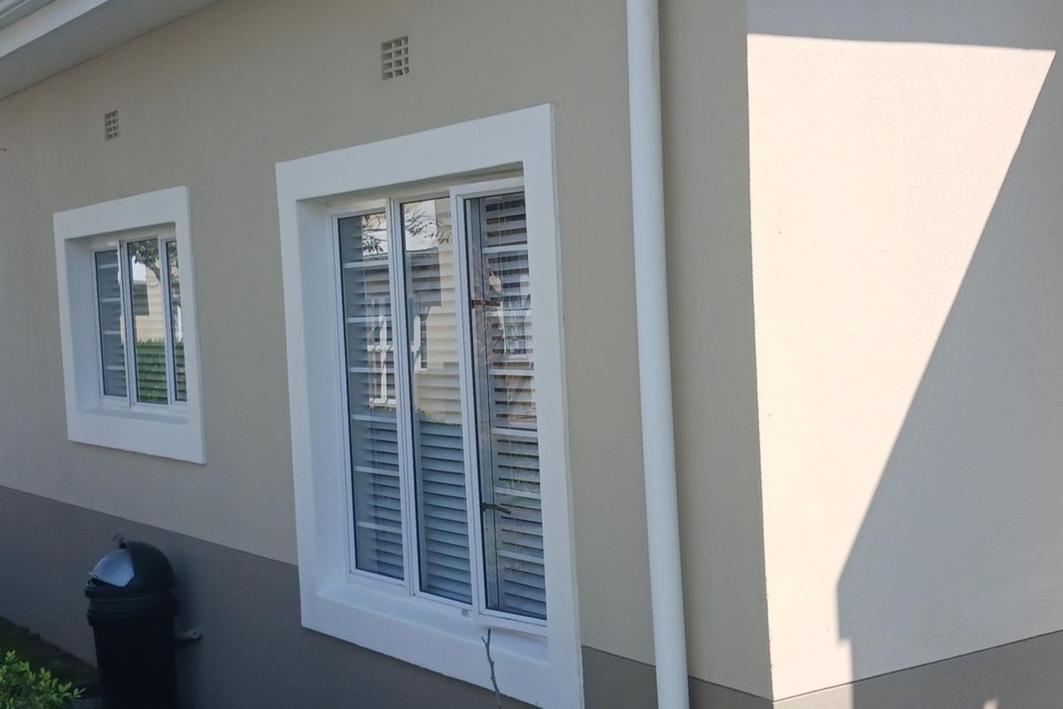 A view of the exterior rear wall of the townhouse, featuring plastered finishes, sliding windows with security bars, and a vertical downpipe.