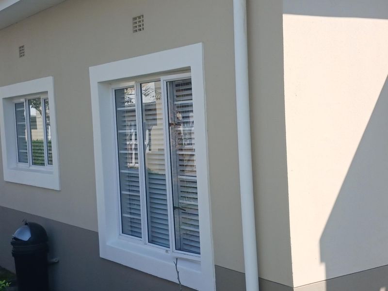 A view of the exterior rear wall of the townhouse, featuring plastered finishes, sliding windows with security bars, and a vertical downpipe.