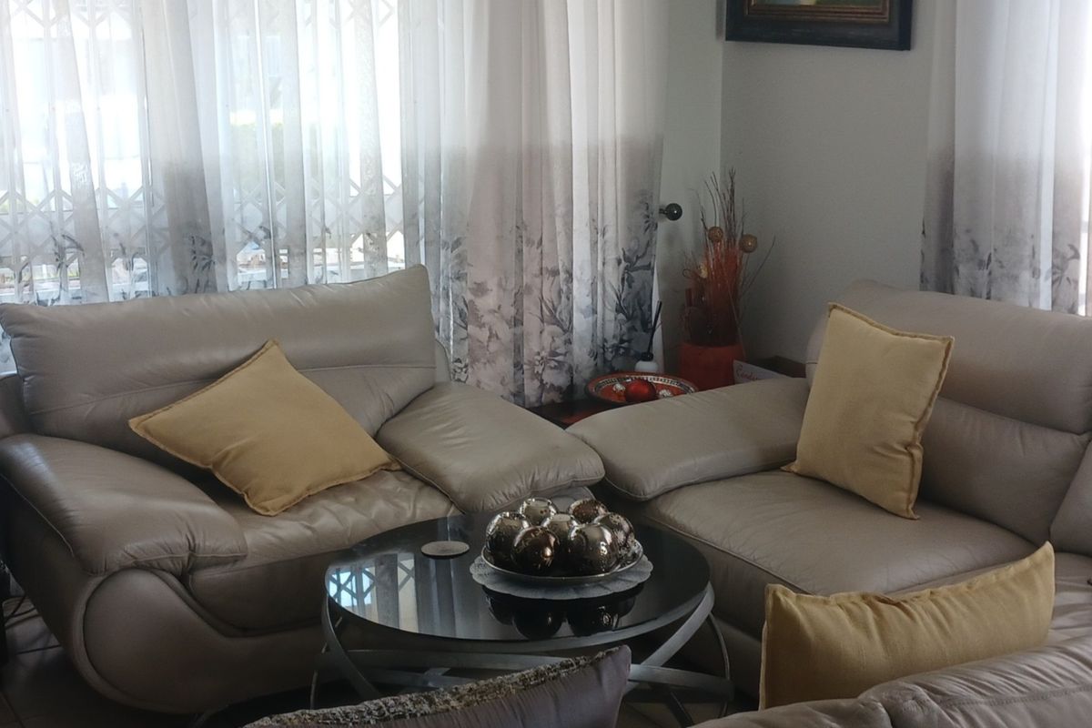 A comfortable living room area featuring tiled flooring and large windows dressed with curtains, providing a bright and functional space.