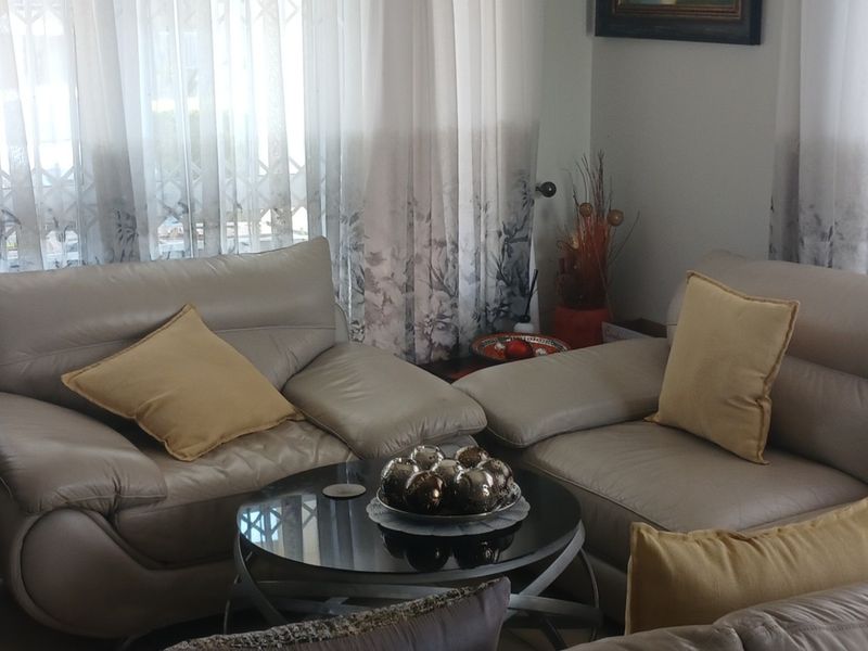 A comfortable living room area featuring tiled flooring and large windows dressed with curtains, providing a bright and functional space.