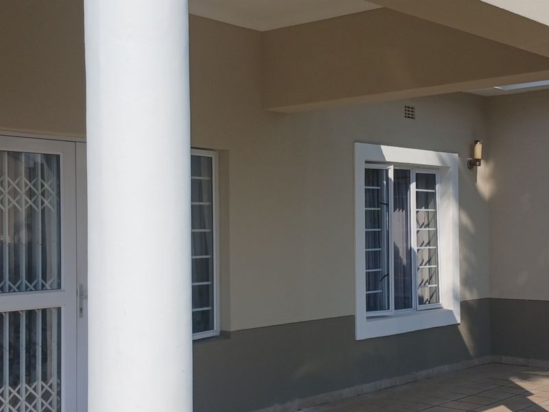 A well-maintained front entrance area featuring a covered patio, structural columns, and secure access points with white window frames and neutral exterior paint.