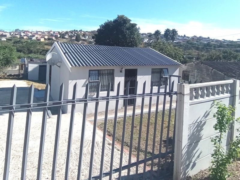 Front view of a detached house featuring a corrugated metal roof, security bars on windows, and a secure perimeter fence with a concrete wall.