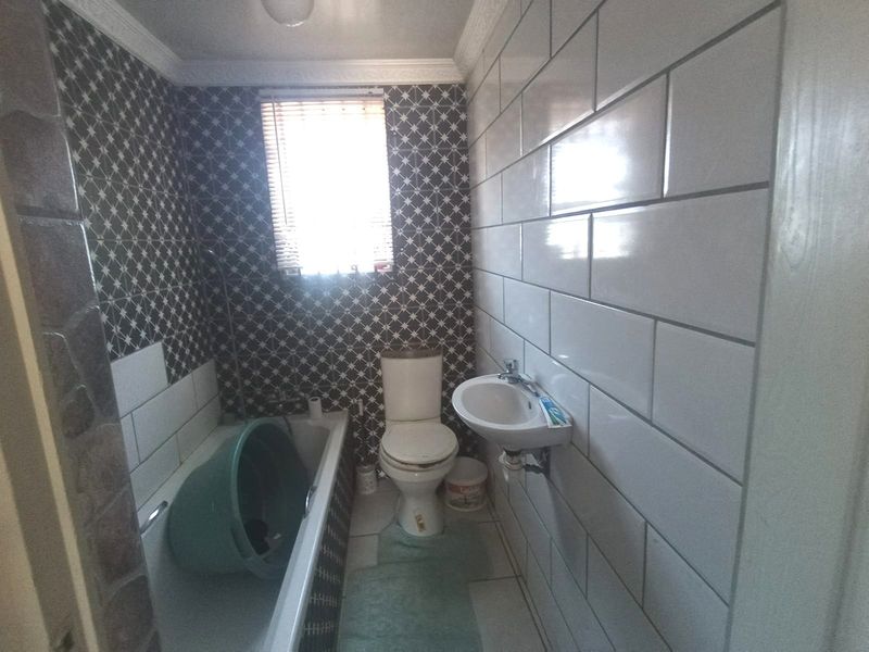 A compact bathroom featuring a bathtub, toilet, and wall-mounted basin with contrasting tiled walls and a window for natural light.