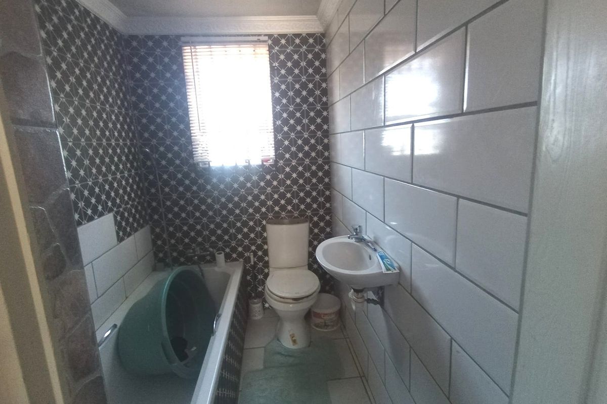 A compact bathroom featuring a bathtub, toilet, and wall-mounted basin with contrasting tiled walls and a window for natural light.