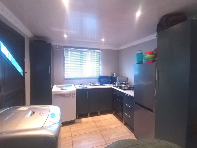 A functional scullery or laundry area featuring built-in cabinetry, a sink, and integrated cooking appliances with tiled flooring and recessed lighting.