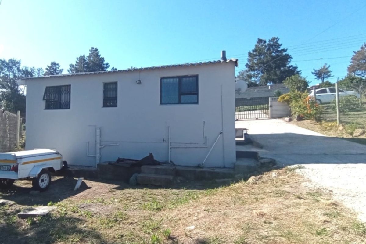 Rear view of the property showing the exterior wall, windows with security bars, and a concrete driveway leading to the rear yard.