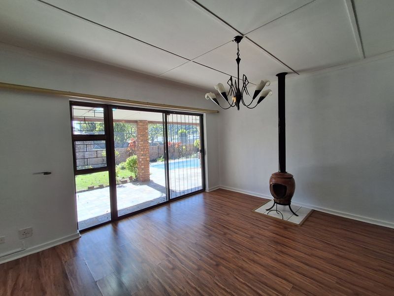 Spacious living room featuring laminate flooring, a freestanding fireplace on a tiled hearth, and sliding glass doors opening to the patio and pool area.