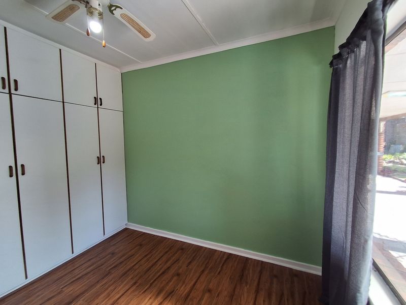 A bright, empty bedroom featuring built-in cupboards, a ceiling fan, and wood-look laminate flooring with a green accent wall.