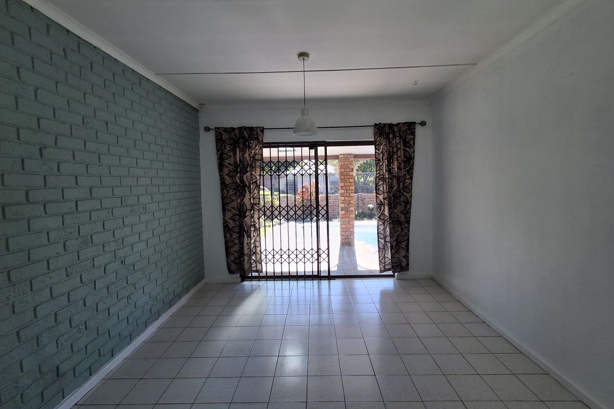 An empty living room featuring tiled flooring, a painted brick accent wall, and a sliding glass door providing access to the outdoor area.
