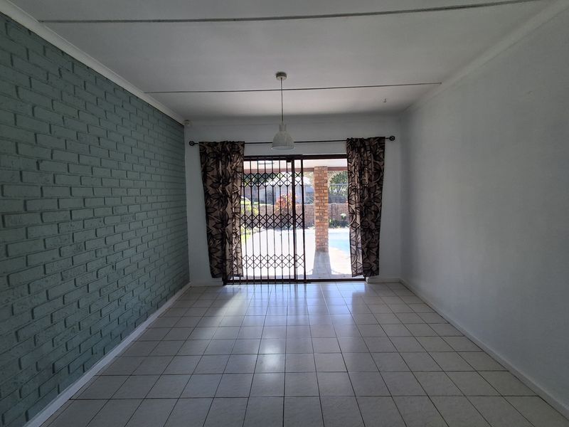 An empty living room featuring tiled flooring, a painted brick accent wall, and a sliding glass door providing access to the outdoor area.