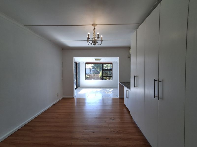 An open-plan living area featuring laminate flooring, built-in storage cabinetry, and a transition to a tiled sunroom space with large windows.