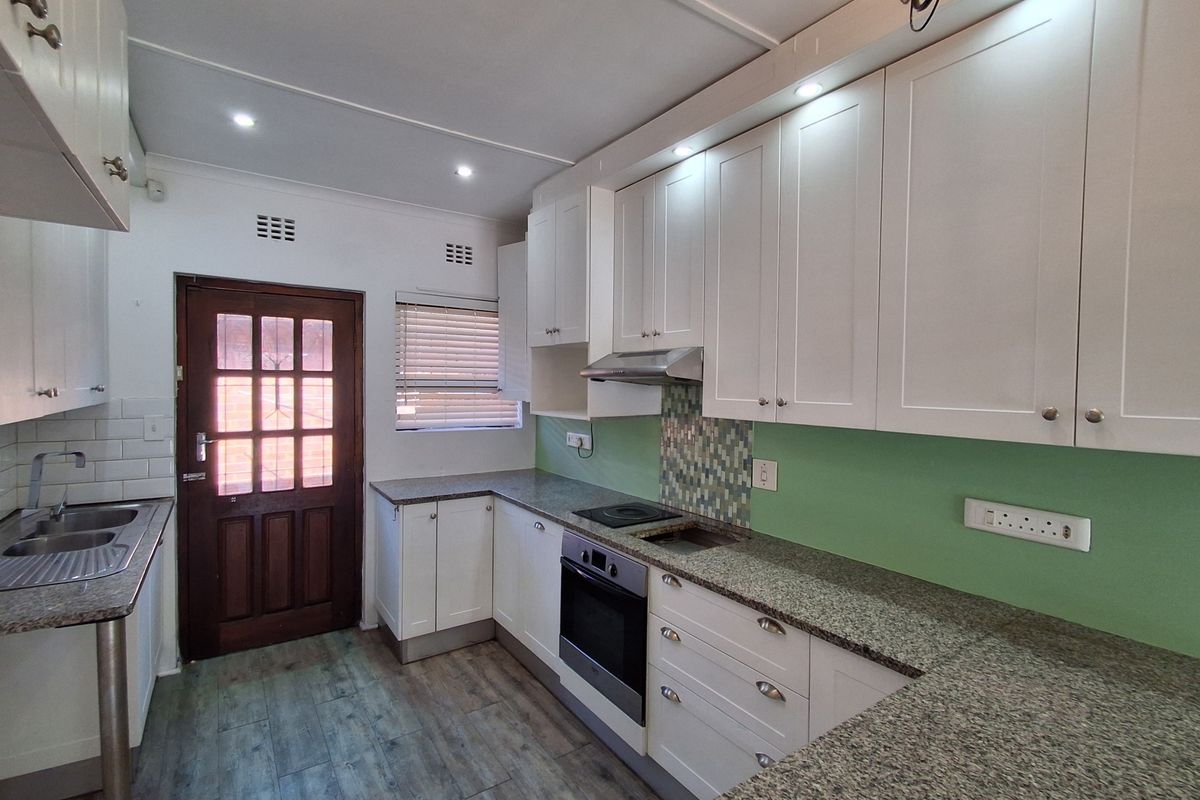 A clean, modern kitchen featuring white cabinetry, granite countertops, integrated appliances, and a mosaic tile splashback with recessed lighting.