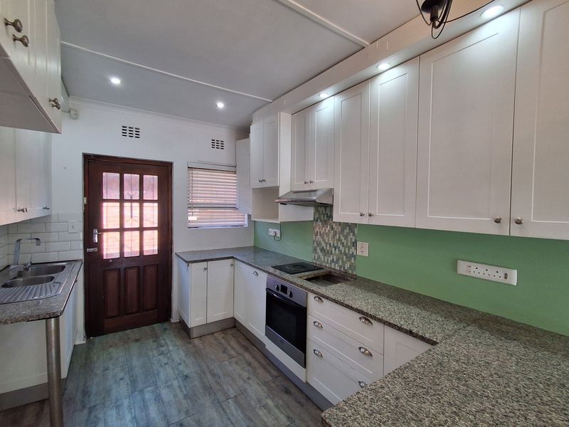 A clean, modern kitchen featuring white cabinetry, granite countertops, integrated appliances, and a mosaic tile splashback with recessed lighting.