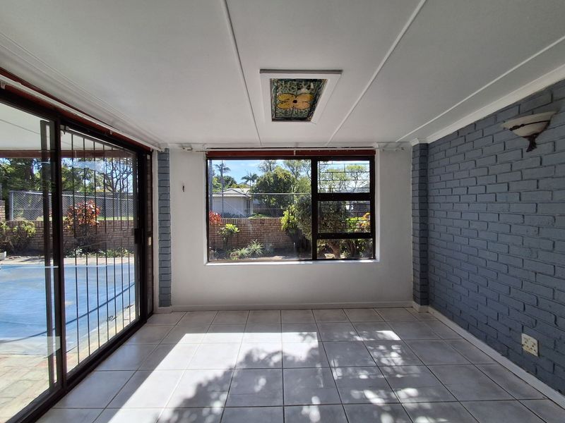 A bright, empty enclosed patio featuring tiled floors, a painted brick feature wall, a skylight, and sliding glass doors overlooking the pool area.