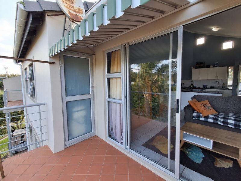 A tiled balcony area featuring a retractable awning, metal safety railing, and sliding glass doors providing access to the interior living space.