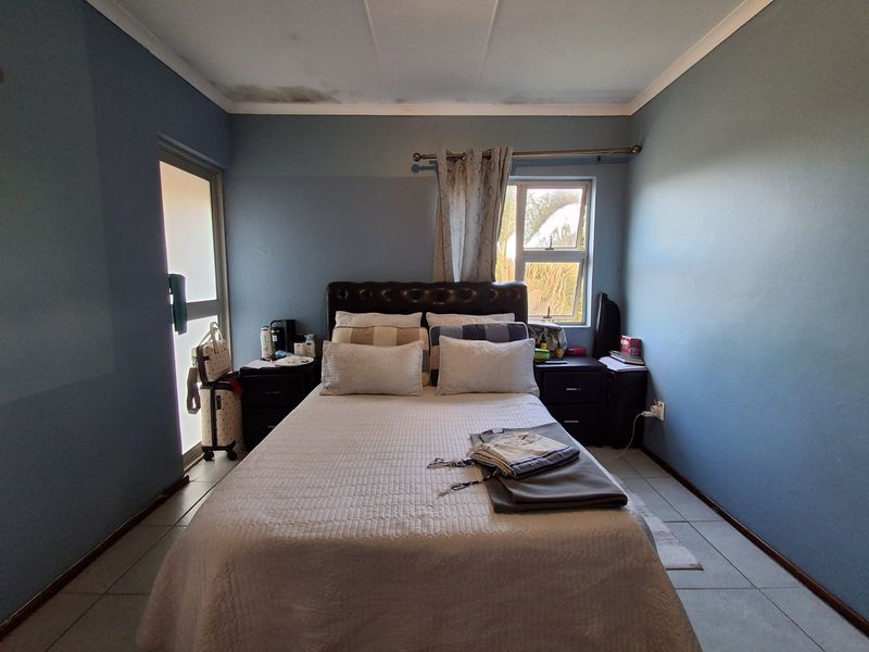 A bedroom featuring tiled flooring, aluminium window and door frames, and visible water staining on the ceiling.