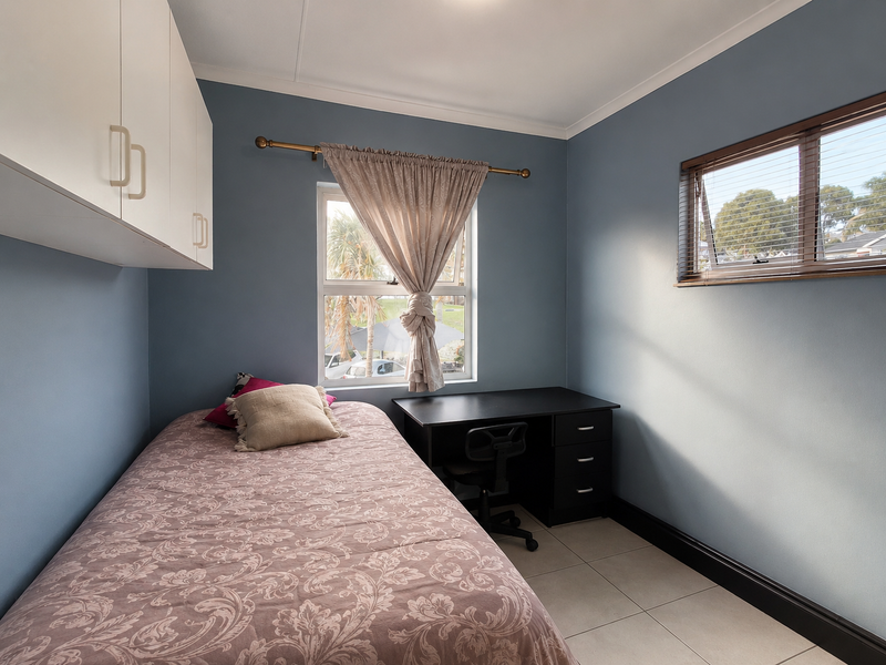 A well-lit bedroom featuring built-in overhead cabinetry, tiled flooring, and dual windows with blinds, offering a functional and comfortable living space.