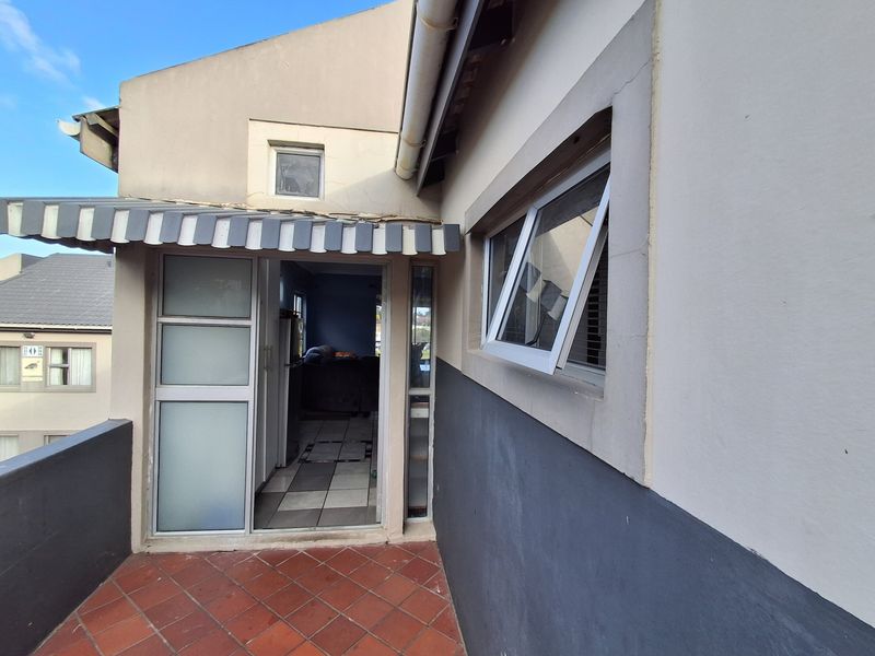 A balcony area featuring terracotta tiling, an overhead awning, and aluminium window and door frames, providing access to the apartment interior.