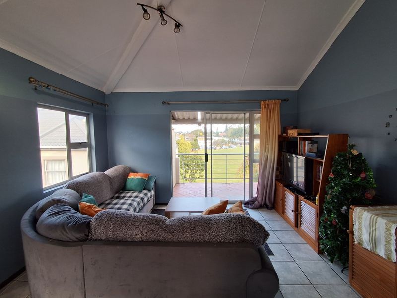 A living room featuring tiled floors, a vaulted ceiling, and sliding glass doors that open onto a balcony with scenic views.