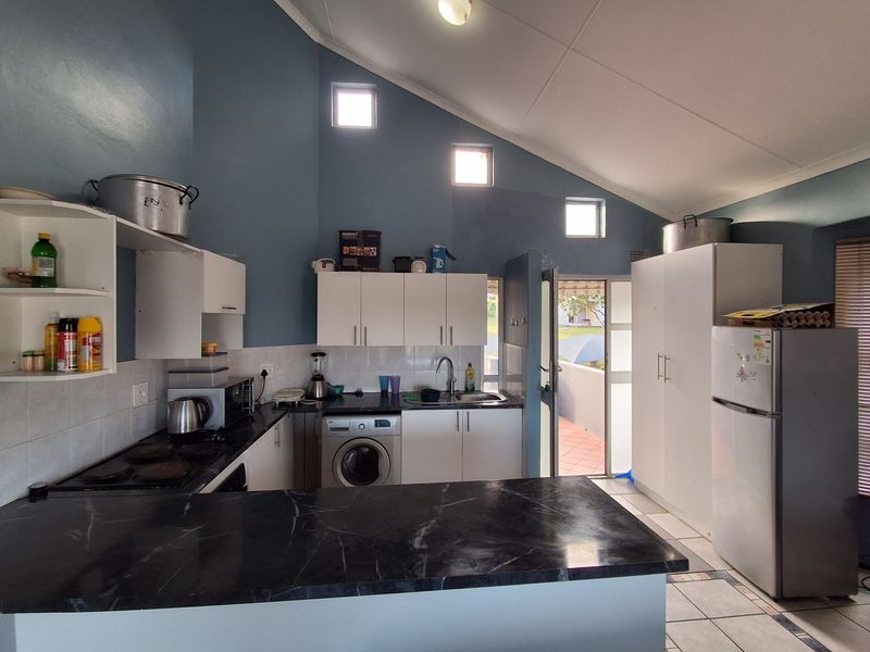 Kitchen featuring vaulted ceilings, built-in cabinetry, dark laminate countertops, and tiled flooring with direct access to an outdoor patio area.
