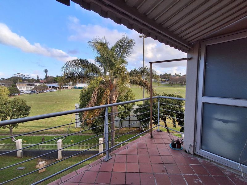 A covered balcony featuring tiled flooring and a metal balustrade, offering an elevated view over the adjacent sports field and surrounding area.