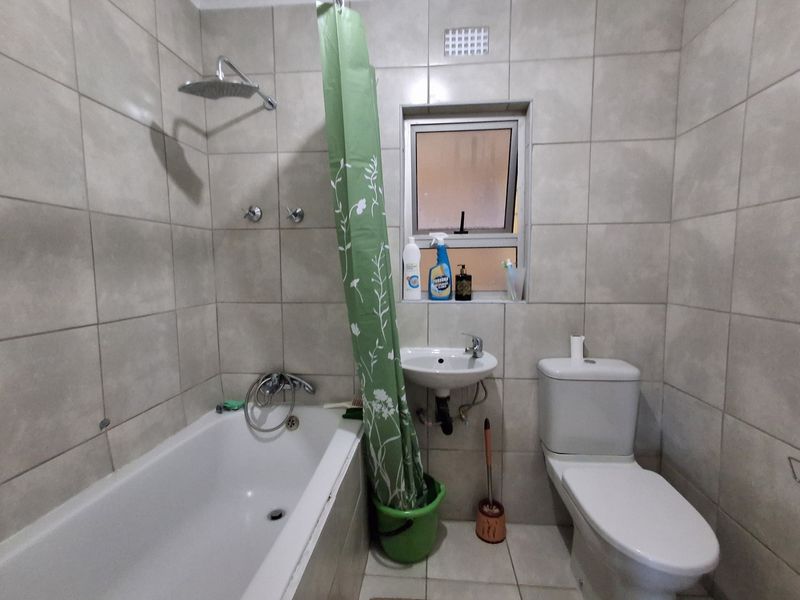 A functional bathroom featuring a bathtub with shower attachment, pedestal sink, toilet, and neutral wall tiling throughout.