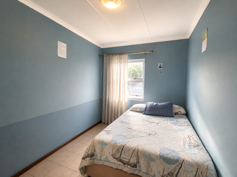 A compact bedroom featuring blue painted walls, tiled flooring, and a window with a curtain rod.