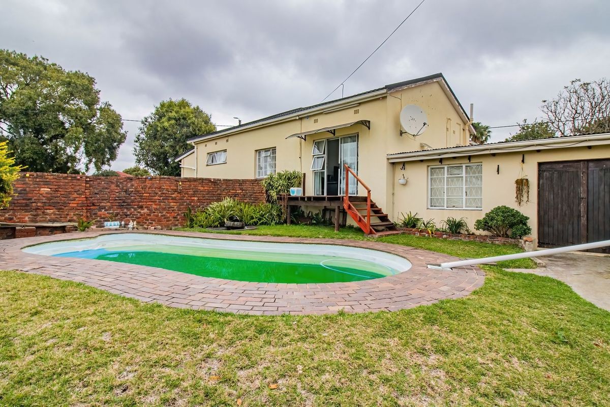 Rear view of the property featuring a swimming pool, raised wooden deck, and a brick boundary wall in a private garden setting.